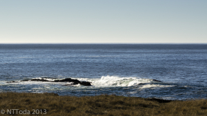 bright sunlit waves break over rock on a calm day